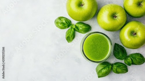 Fresh green apples, basil leaves, and a glass of green juice on a light background.