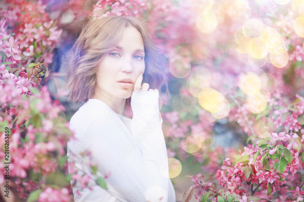 Fototapeta premium Springtime background, a woman in pink in a blooming cherry orchard, a model posing in a romantic style