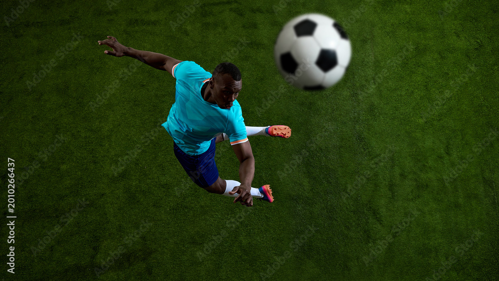 Fototapeta premium Overhead soccer player striking flying ball on green field background. Concept of football action, powerful shot, sports poster design, match promotion and athletic gear campaign.