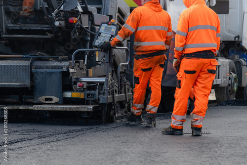Foto Road workers lay asphalt on a busy street in the morning while operating heavy e
