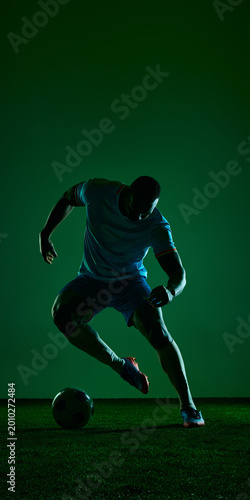 Foto Soccer player dribbling ball in dark green studio sport scene