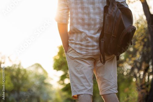 Obraz na plátně Man tourist traveler with backpack standing against green environment in sunset, symbolizing harmony and deep connection with nature during his journey, solo walking and leasure