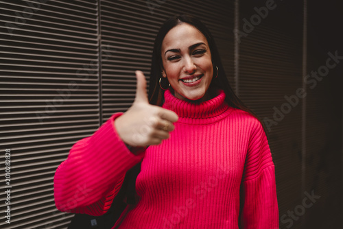 Fotografie Cheerful student girl gesturing like or thumb up with a big smile outdoors, caucasian model in bright pink sweater recommending service or product, positive expression of success and agreement