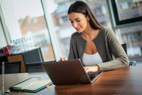 Free Download Confdient businesswoman wearing business casual and and using laptop in a modern bright office - GFXLoad