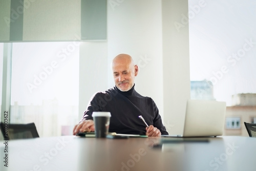 Mid-aged businessman sitting in a meeting room table and working on laptop