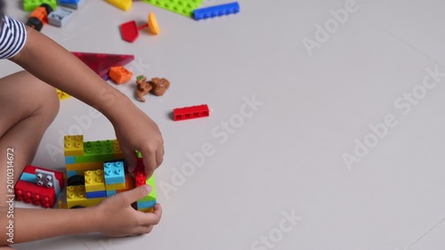 Child playing with colorful plastic building blocks on the floor, hands assembling toy bricks, early learning, creativity, motor skills development, education concept, playful childhood activity.