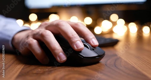 Close-up of a hand using a computer mouse on a wooden desk with blurred lights in the background