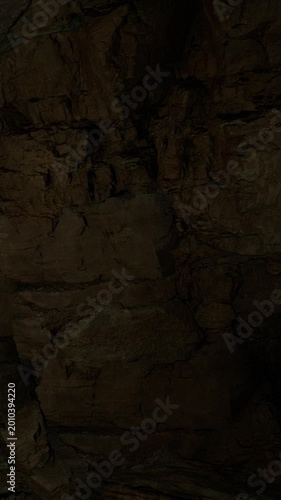The scene shows the inside of a cave with rough stone walls. Shadows fill the space, creating a dark environment. The cave appears natural with no signs of human presence.
