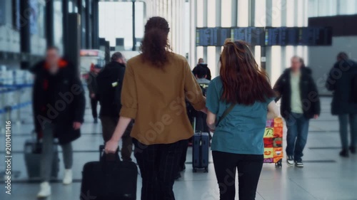A couple races through a bustling airport terminal, checking the gate information on screens as they run.