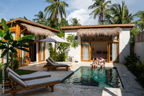 Couple sitting at the edge of a swimming pool enjoying their private tropical villa