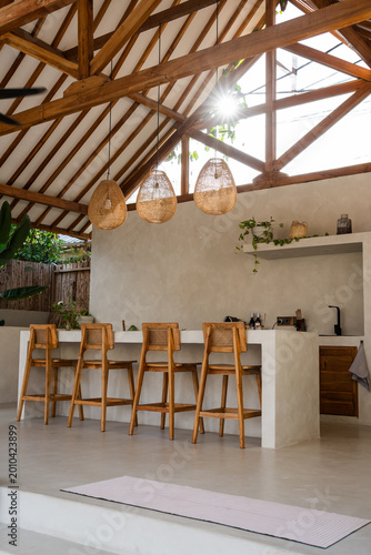 Modern outdoor kitchen with concrete counter, wooden beams, bar stools and natural light