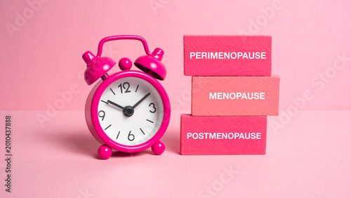 Tableau sur toile Pink alarm clock next to wooden blocks labeled with perimenopause menopause and postmenopause stages representing the biological clock