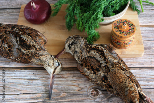Fotografía Two woodcocks lie on a cutting board next to a salt shaker, red onion and fresh dill