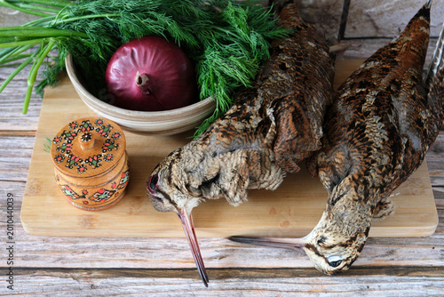 Fotografie Two woodcocks lie on a cutting board next to a salt shaker, red onion and dill