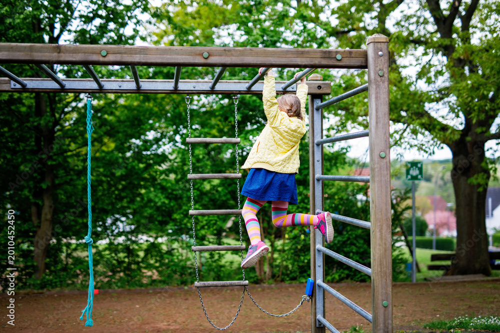 Fototapeta premium Little girl doing gymnastics on a climbing frame, horizontal bar on school yard. Child enjoying school break.