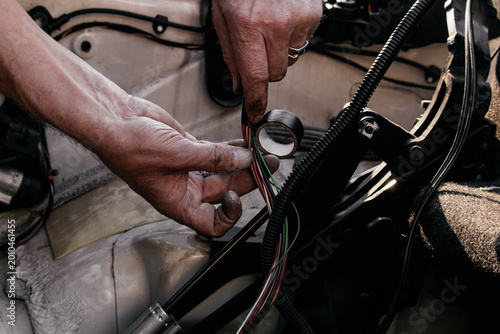 Tableau sur toile Auto electrician insulating a wiring harness with black electrical tape during a convertible roof mechanism repair