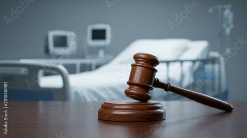 Wooden judge gavel on a table in a hospital room with a patient bed and medical equipment in the background