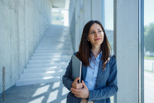 Businesswoman holding laptop looking away in modern office