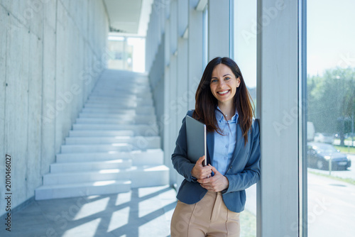 Confident businesswoman smiling and holding laptop in modern office building
