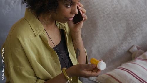 Medium handheld shot of young Black mother calling on mobile phone while holding pills and looking after small son in living room
