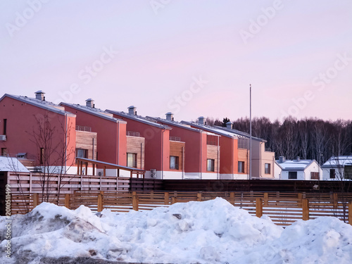 Rows of houses stand in a neighborhood covered with snow. The sky shows signs of sunset