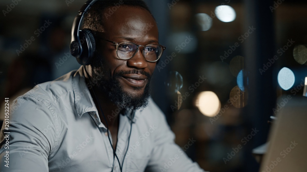 Fototapeta premium Professional man wearing headphones and glasses at night. Customer service, tech support, and remote work concept.