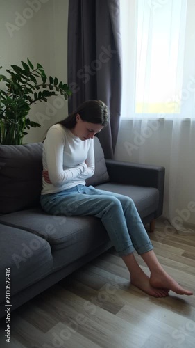 Flatulence ulcer young woman sitting on sofa holding on belly, stomach pain from food poisoning, abdominal pain and digestive problem, gastritis or diarrhea. Abdomen inflammation, menstrual period