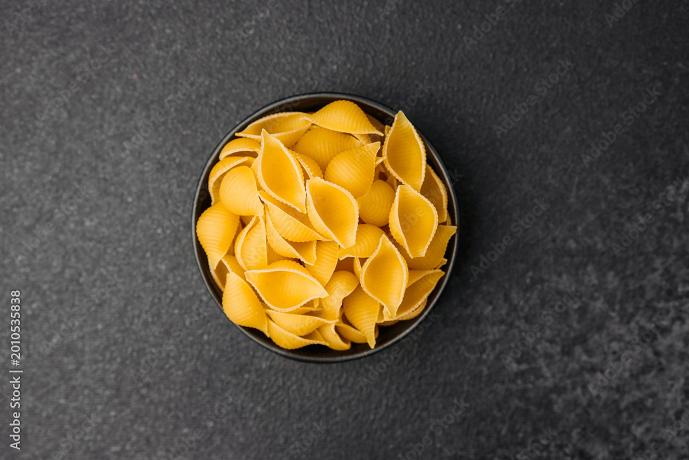 Fototapeta premium Different shapes of uncooked pasta arranged in a bowl on a dark surface