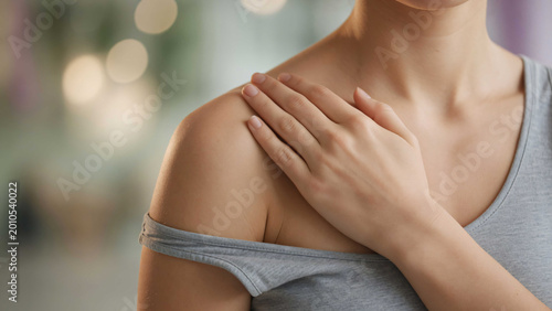 Woman with hand on shoulder wearing gray off shoulder shirt in blurry background