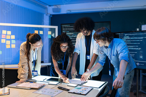 Diverse group of technical experts analyzing creative sketches on table in office. Young professional team collaborating on software development and project planning during meeting
