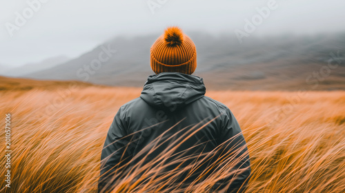 Rear view of a traveler standing in a windy golden field with mountains in the background, capturing solitude, adventure, freedom, and exploration in nature.