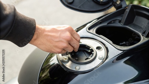 A person’s hand is opening the fuel cap on a black motorcycle’s fuel tank.