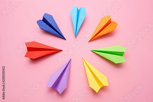 Colorful paper airplanes arranged in a circle on pink background