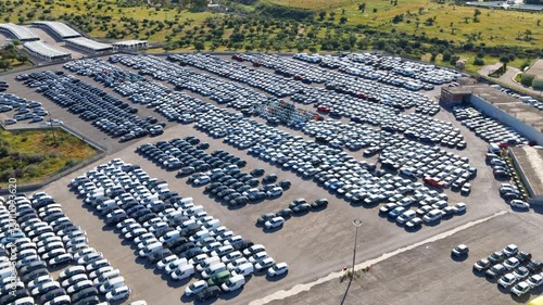 Cinematic forward drone shot over a massive automotive storage terminal. Thousands of new cars parked in neat rows highlight global supply chain and industrial logistics.