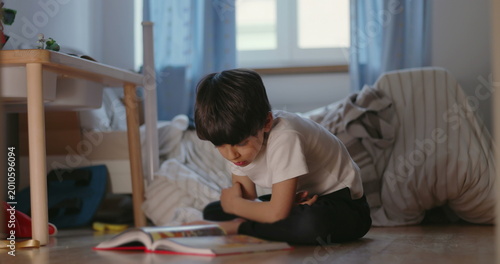Fotografía Boy reading book sitting on bedroom floor, quiet childhood moment of learning, i