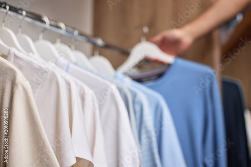Hand selecting a blue t-shirt from a collection of clothes hanging on a rack in a closet or retail store