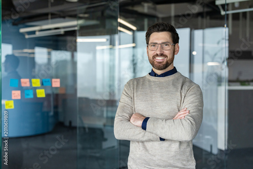 Foto Confident business man wearing glasses and a sweater, standing with arms crossed