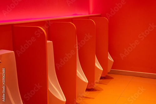 Red public bathroom with rows of urinals