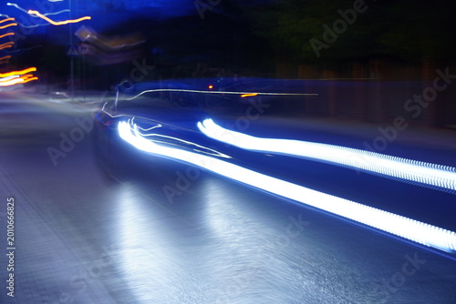 Tableau sur toile An evening shot of a car in motion with subtle motion blur, where the headlights create distinct light trails while the vehicle's shape remains visible against the twilight