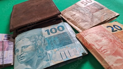 Schilderij op canvas Brown leather wallet resting on a green surface alongside various denominations