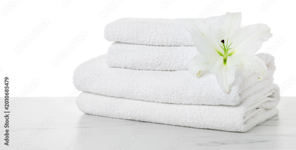 Obraz premium Stacked terry towels and lily flower on marble table against white background