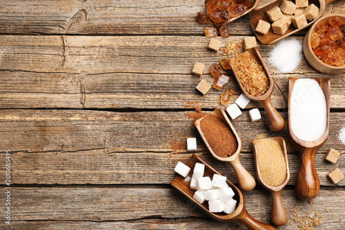 Fotografia Different types of sugar in scoops on wooden table, flat lay