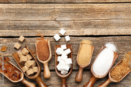 Quadro su tela Different types of sugar in scoops on wooden table, flat lay