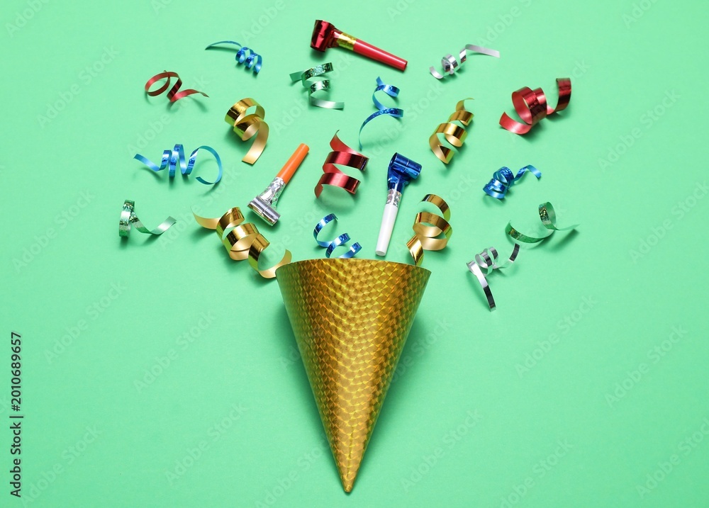 Naklejka premium Shiny party streamers, horns and cone on green background, flat lay