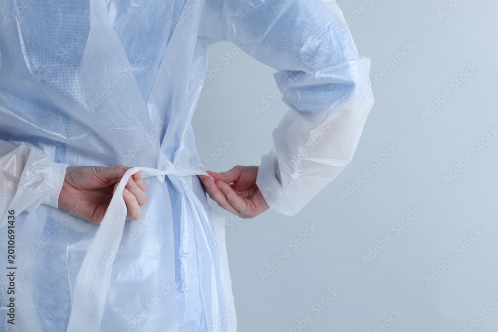 Fototapeta premium Medical worker tying disposable isolation gown on light background, closeup