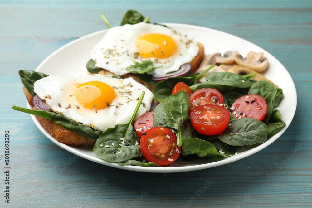 Fototapeta premium Fried eggs, bread, spinach, tomatoes and mushrooms on light blue wooden table, closeup