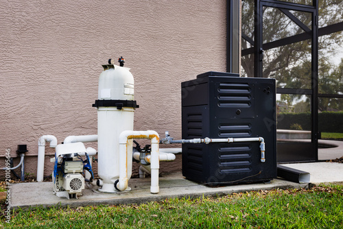 Fotografie Modern natural gas swimming pool heater unit and pool water filtration equipment on concrete slab outside of house