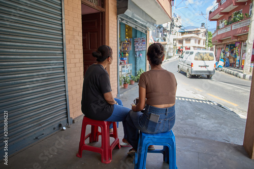 Two Women Sitting on Colorful Plastic Stools, Engaging in Conversation While Enjoying a Sunny Day in an Urban Street Setting