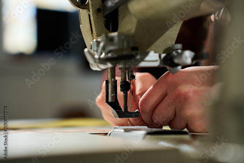 Artisan hands threading a heavy-duty industrial sewing machine in a workshop.