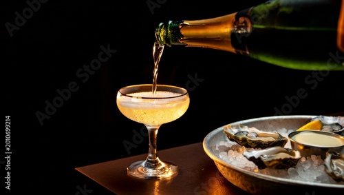 Sparkling drink filling a coupe glass, accompanied by fresh oysters on ice, a lemon wedge, and sauce